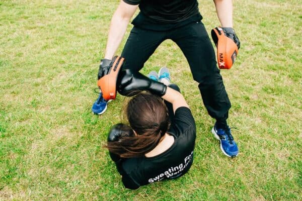 Personal trainer holding pads while client performs alternating boxing punches during an outdoor workout.