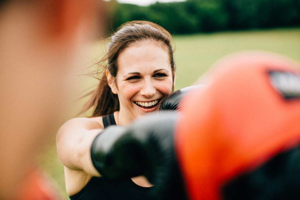 Client smiling and throwing a punch during a boxing-inspired outdoor personal training session.