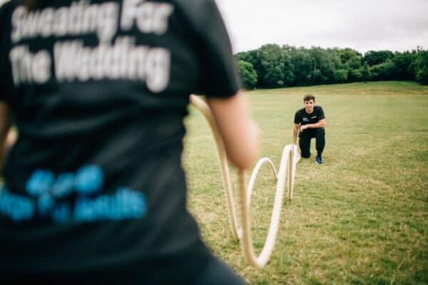 Client using battle ropes during an outdoor personal training session in Essex park, with mobile PT coaching in background